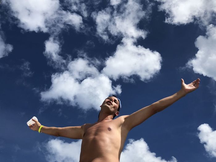 Low angle view of shirtless man with arms outstretched against sky