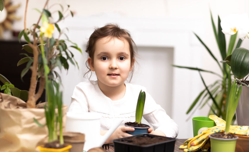 Portrait of cute girl holding plant on table at home
