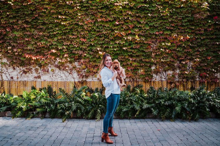 Full length portrait of smiling young woman standing against plants