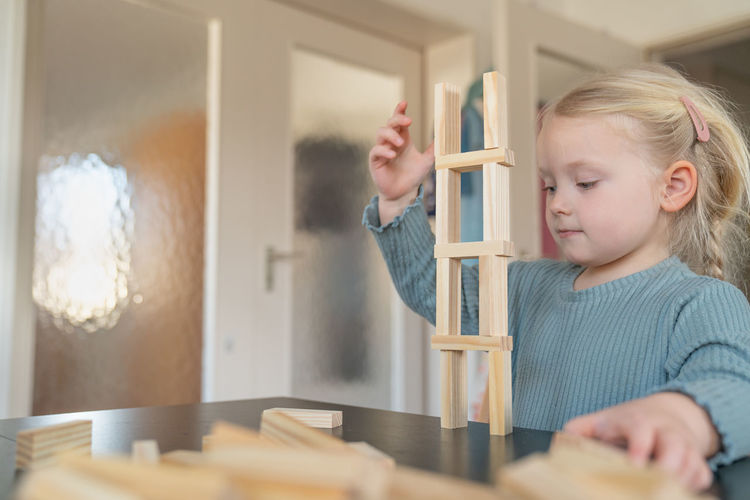 A toddler girl is building a house from wooden bricks