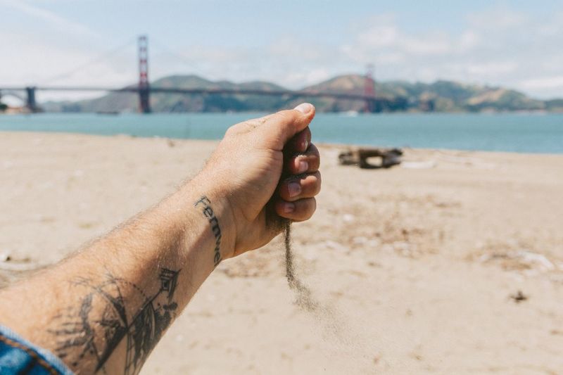 Cropped image of hand holding sand with golden gate bridge in background