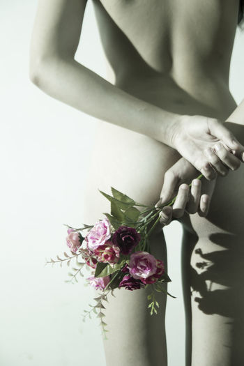 Midsection rear view of woman holding flowers while standing against wall