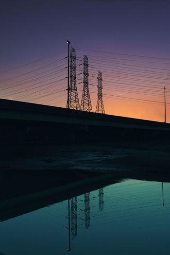 Silhouette electricity pylons against sky during sunset
