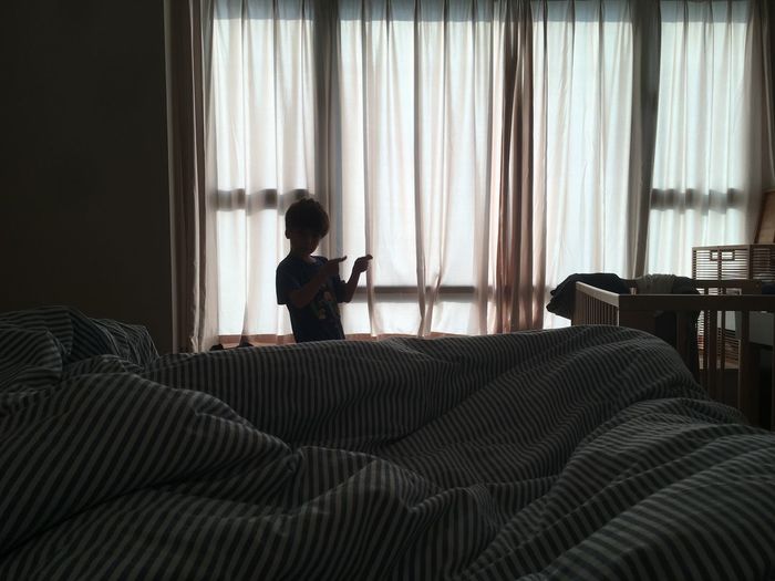 Boy gesturing while standing by bed at home