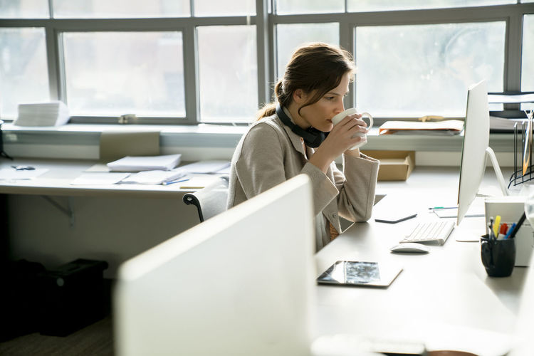 Side view of businesswoman having drink while working at desk in office