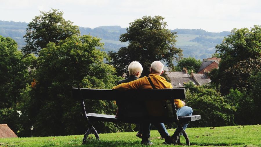 Rear view of senior couple sitting on bench against sky