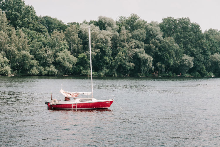 Boat sailing on river by trees against sky