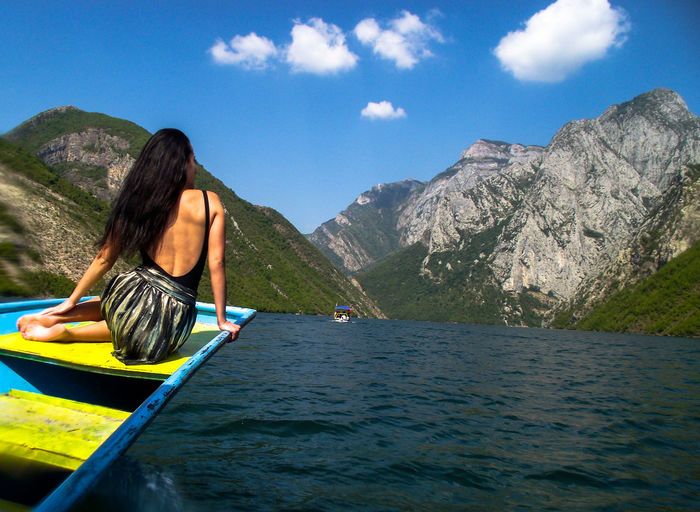 Rear view of woman sitting on boat in lake against sky