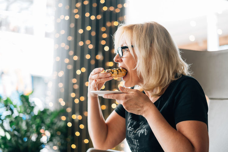 Mature woman eating donut at cafe