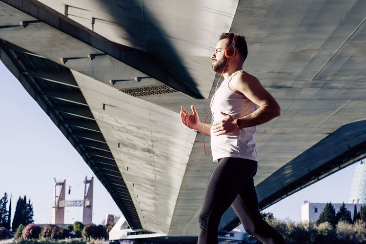 Side view of man listening music while jogging in city