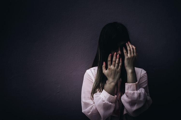 Portrait of young woman covering face with halloween make-up against wall