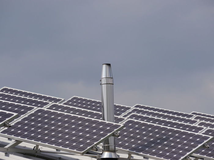 Low angle view of chimney and solar panels against sky