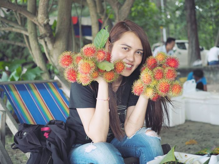 Portrait of smiling woman holding rambutans while sitting on lounge chair