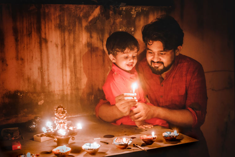 Father and son lighting diyas at night