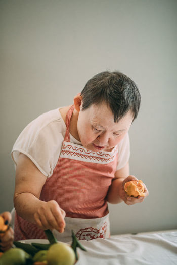 Elderly woman with down syndrome is studying in the kitchen peels tangerines