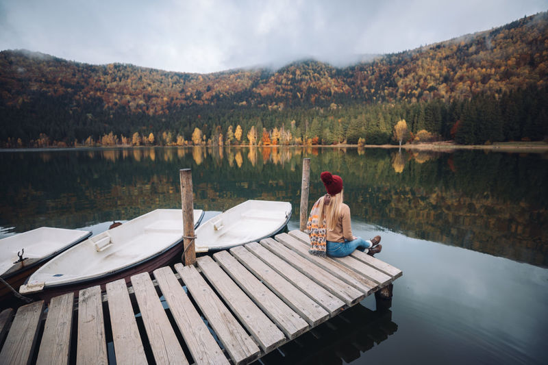 Traveler girl with relaxing by autumn foggy lake at sunrise. young woman sitting on pier 