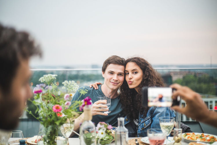 Cropped hand of man clicking photograph of couple through phone on terrace during party