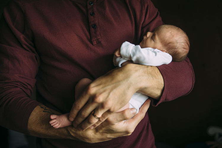 Midsection of father carrying cute sleeping daughter at home