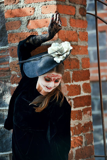 Woman wearing halloween mask against brick wall