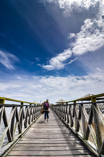 Rear view of man walking on footbridge against sky