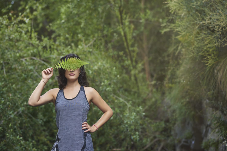 Woman with a fern on her face. she is in a river and covers half of her face with a fern leaf.