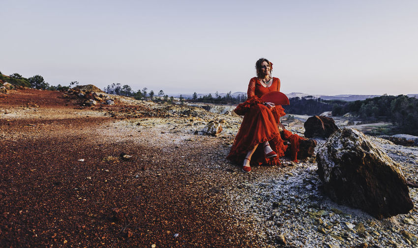 Woman sitting on stone against clear sky