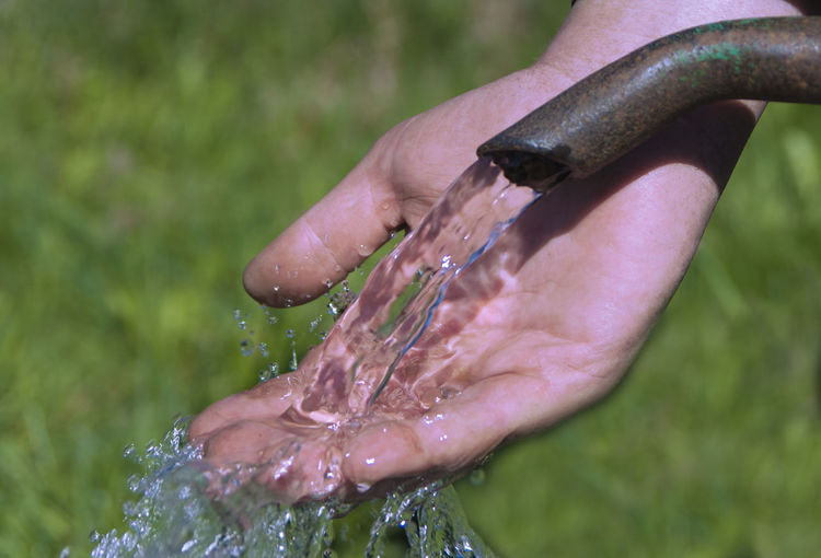 Cropped hand touching water flowing from pipe
