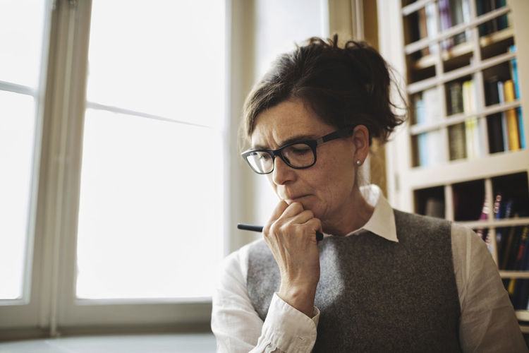 Female professional with hand on chin by window in law library