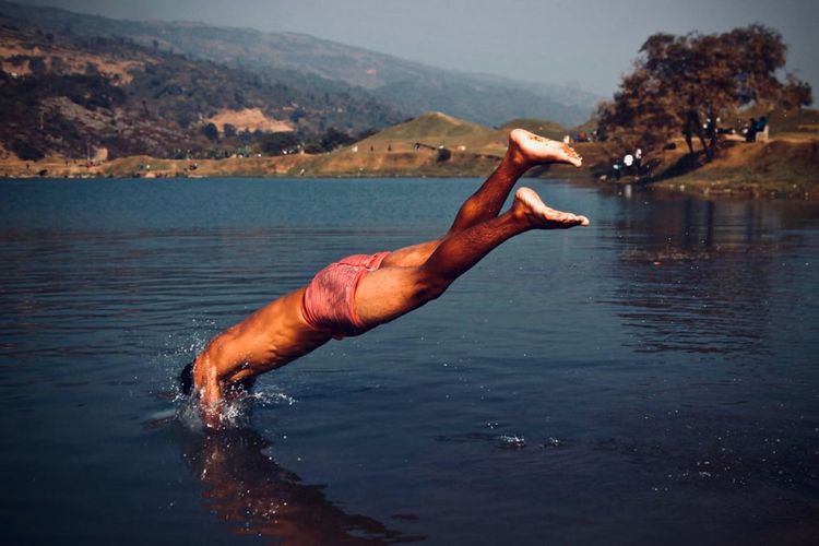 Full length of shirtless man jumping in lake