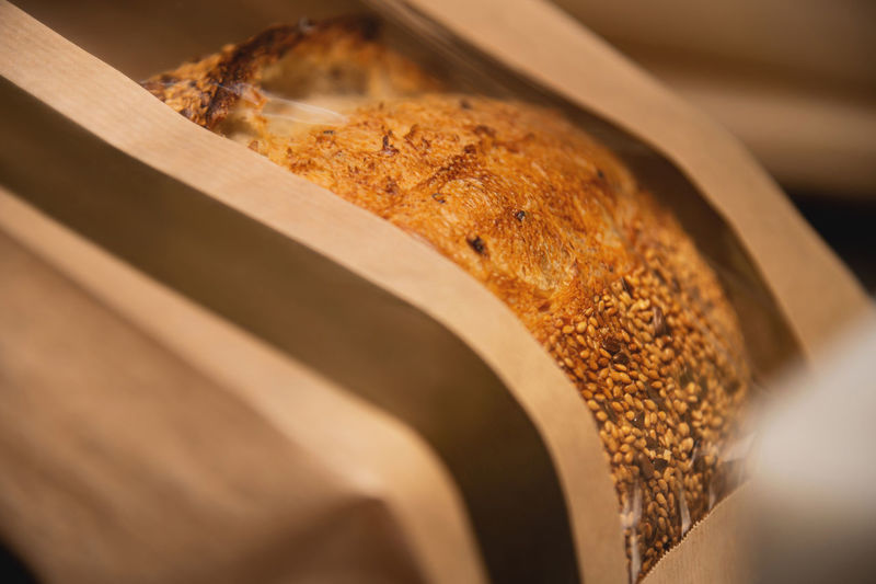 A loaf of white artisan hot bread in a paper bag with transparent inserts on a white background