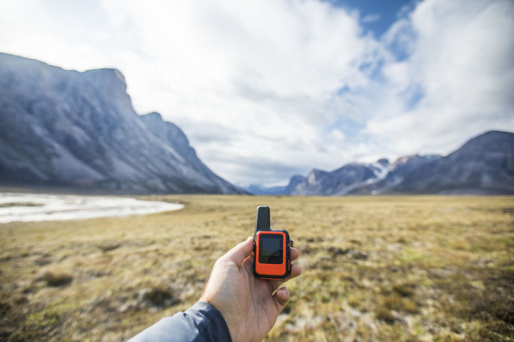 Hand holding smart phone against mountain range