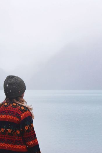 Rear view of woman looking at lake during foggy weather