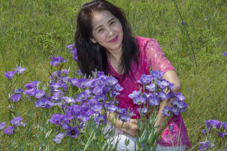 Portrait of a smiling young woman with purple flowers in field
