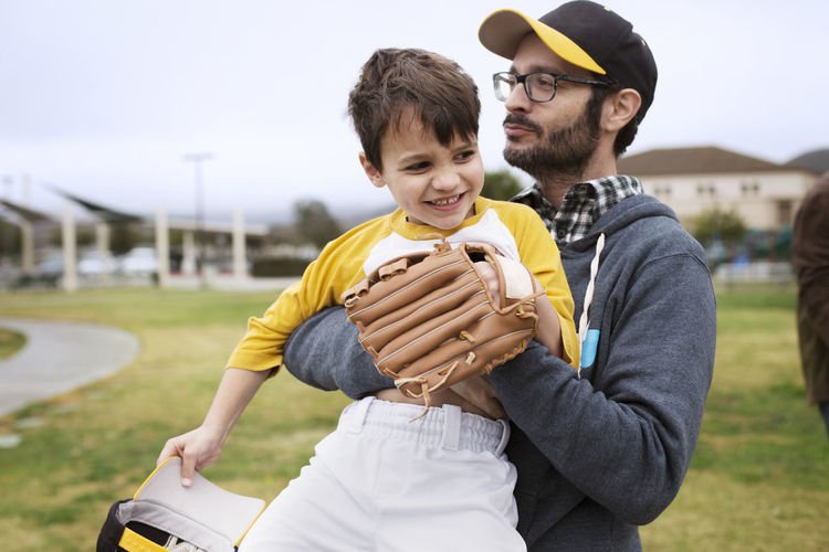 Father carrying happy son while standing on sports field