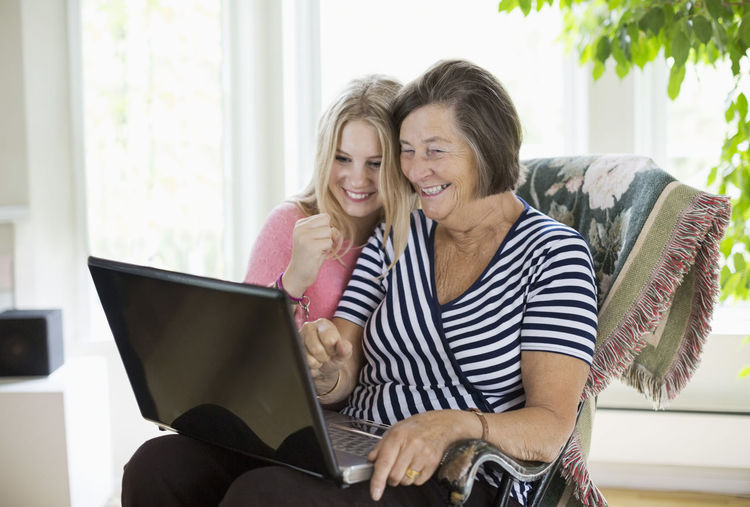 Happy grandmother and granddaughter using laptop at home