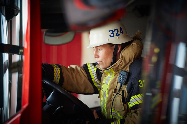 Female firefighter wearing helmet sitting in fire truck at fire station