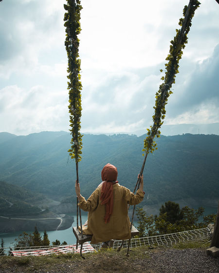 Rear view of woman sitting on swing against mountains
