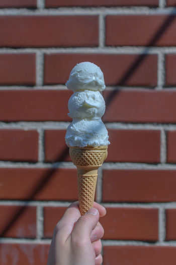 Hand holding ice cream against brick wall