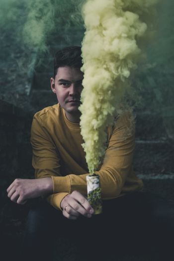 Portrait of young man holding smoke bomb while sitting on steps