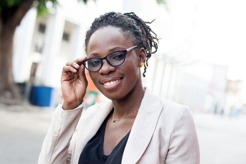 Portrait of a smiling young woman grabbing her glasses outdoors.