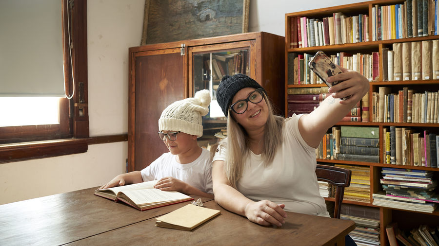 Blonde mother with her son taking selfie smiling in a large public library.