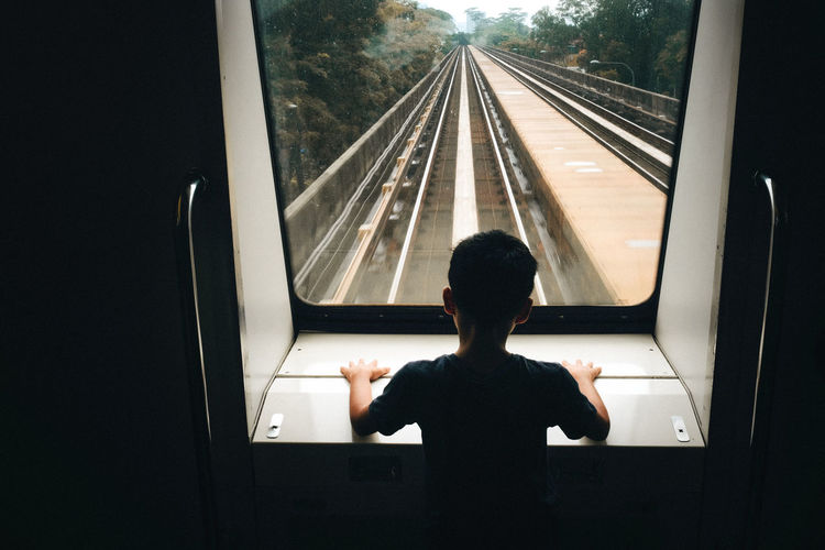 Rear view of boy looking through window in train