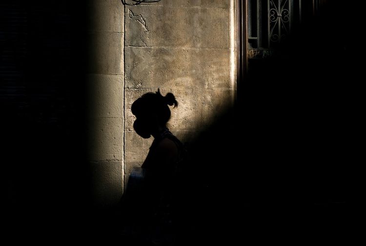 Side view of silhouette woman walking un front of a  sunstruck wall.
