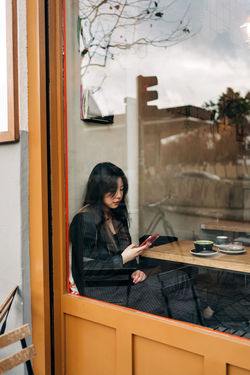 WOMAN SITTING ON TABLE BY WINDOW AT OFFICE