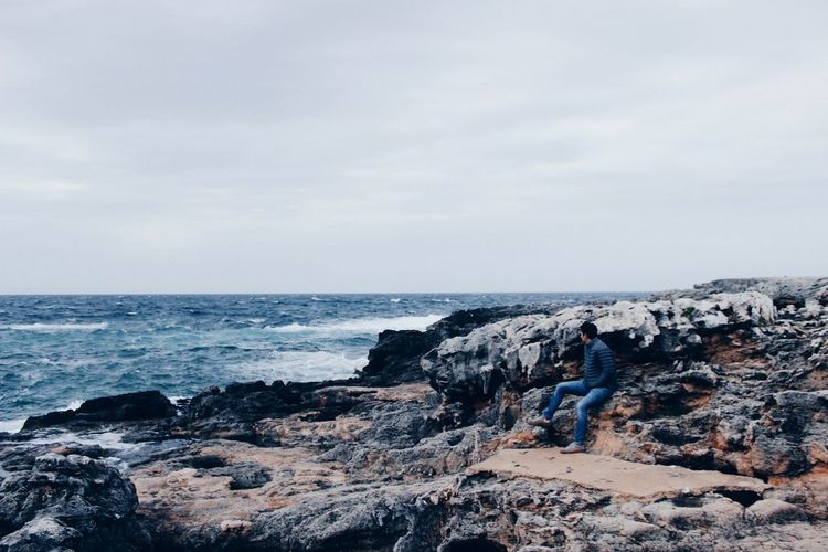 Man looking at sea while sitting on rock formation 