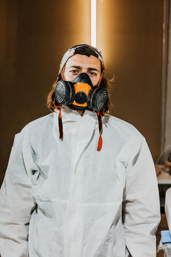 Male worker wearing safety respirator and protective costume in workshop while looking at camera