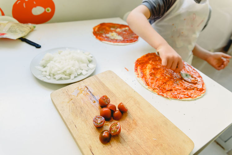 Midsection of boy making pizza on table at home