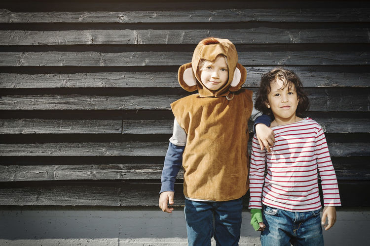 Girl in monkey suit standing with friend against black wooden wall