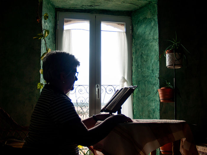 Woman reading book while sitting by window at home