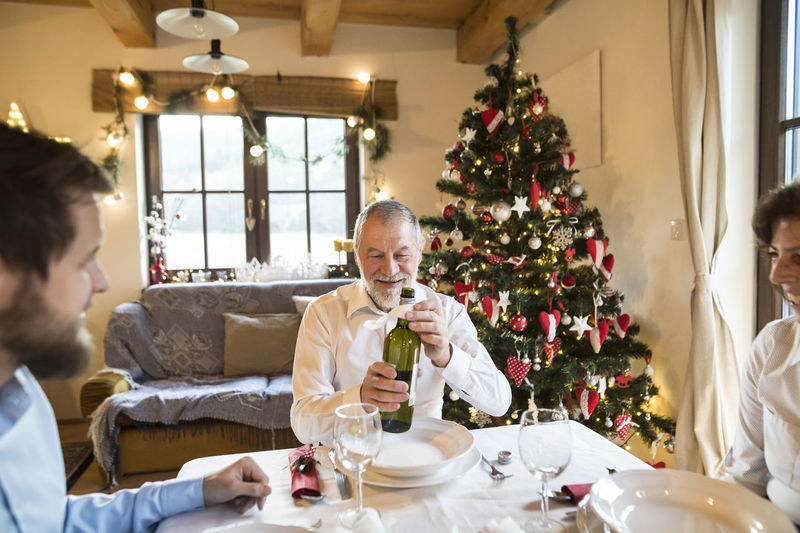 Smiling senior man with family holding bottle of wine at christmas dinner table